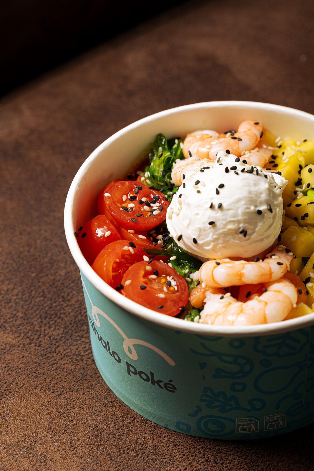 Bowl Mahalo Poké con langostinos, burrata, mango y cherry sobre superficie de cuero marrón