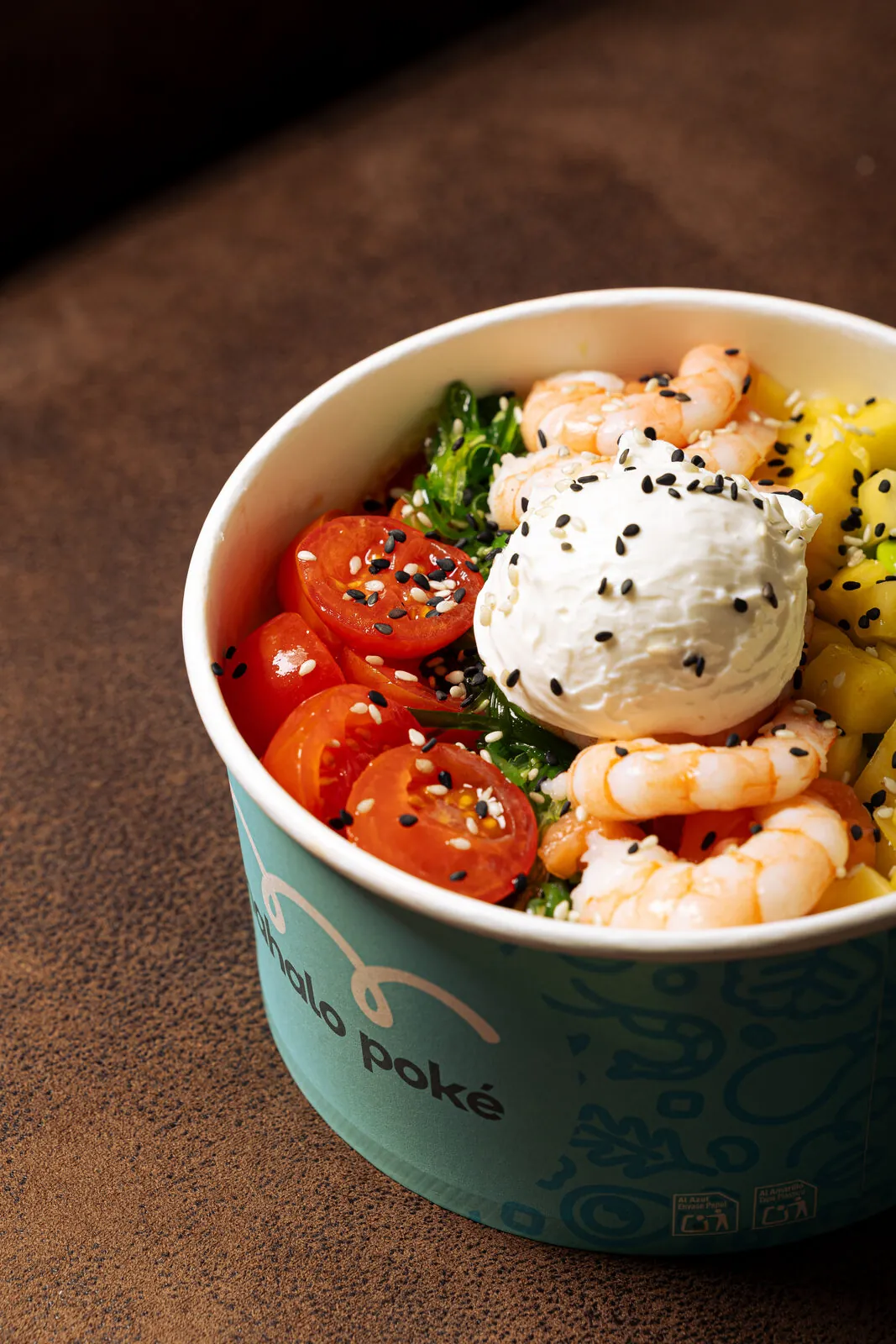 Bowl Mahalo Poké con langostinos, burrata, mango y cherry sobre superficie de cuero marrón