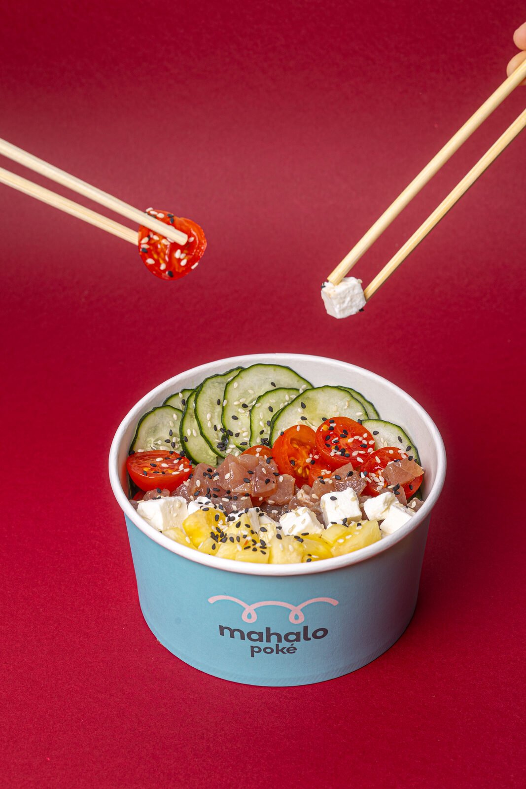Bowl Mahalo Poké sobre fondo rojo intenso con palillos suspendidos