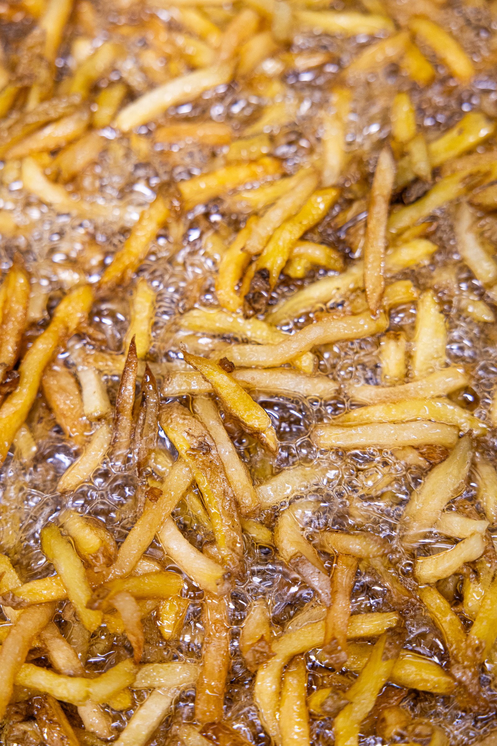 Patatas friéndose en aceite hirviendo, primer plano