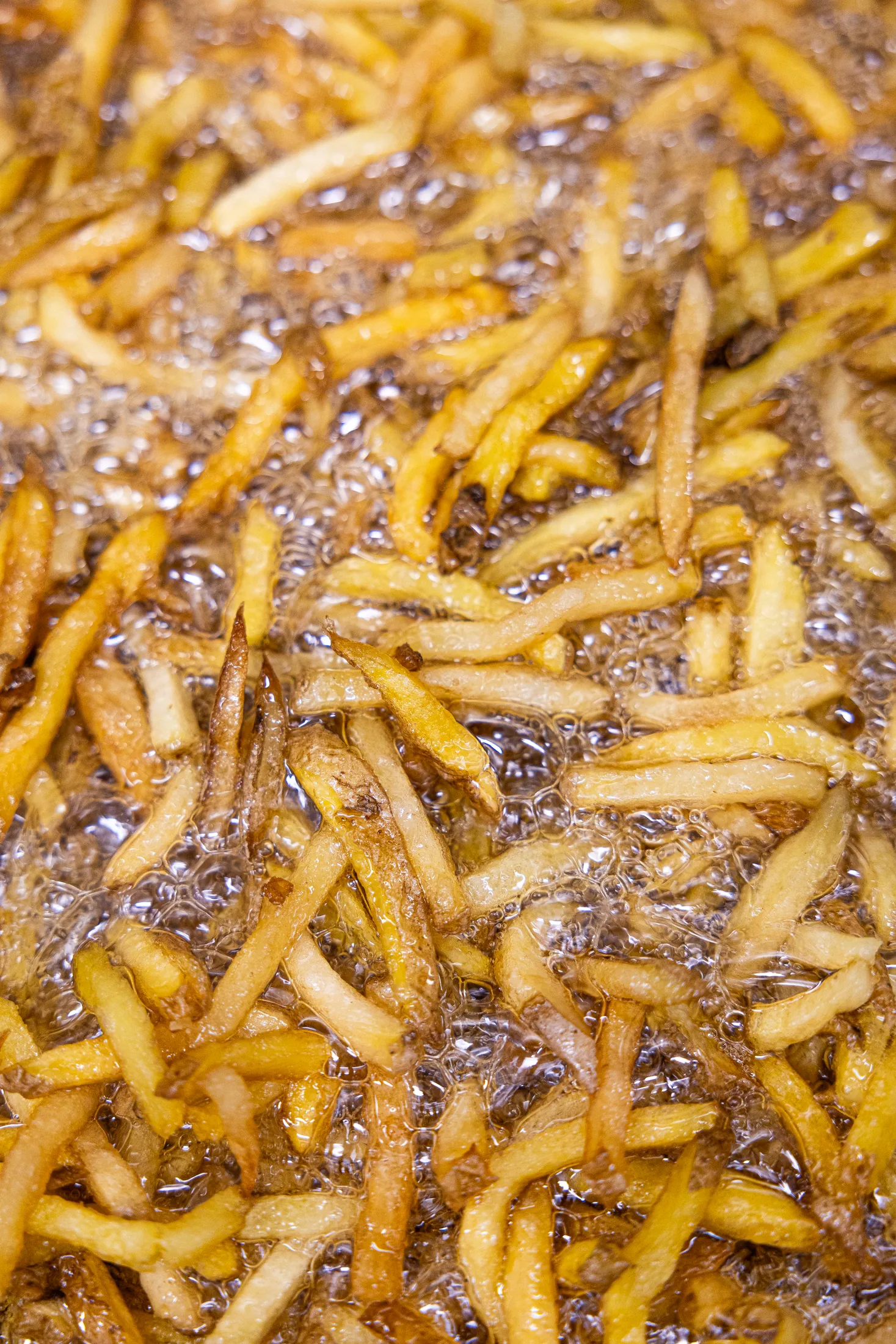 Patatas friéndose en aceite hirviendo, primer plano
