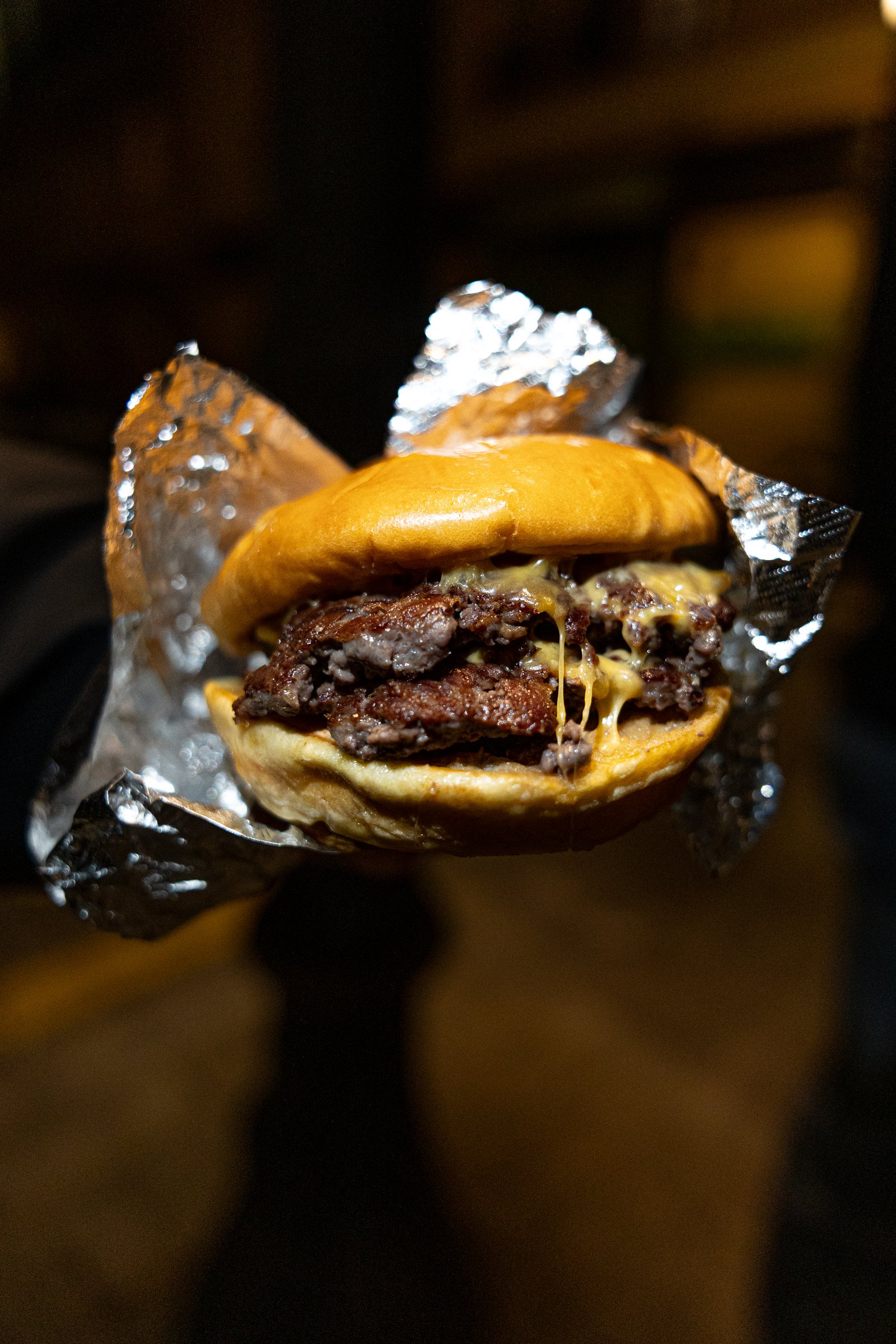 Smash burger envuelta en aluminio sostenida con la mano, encuadre vertical