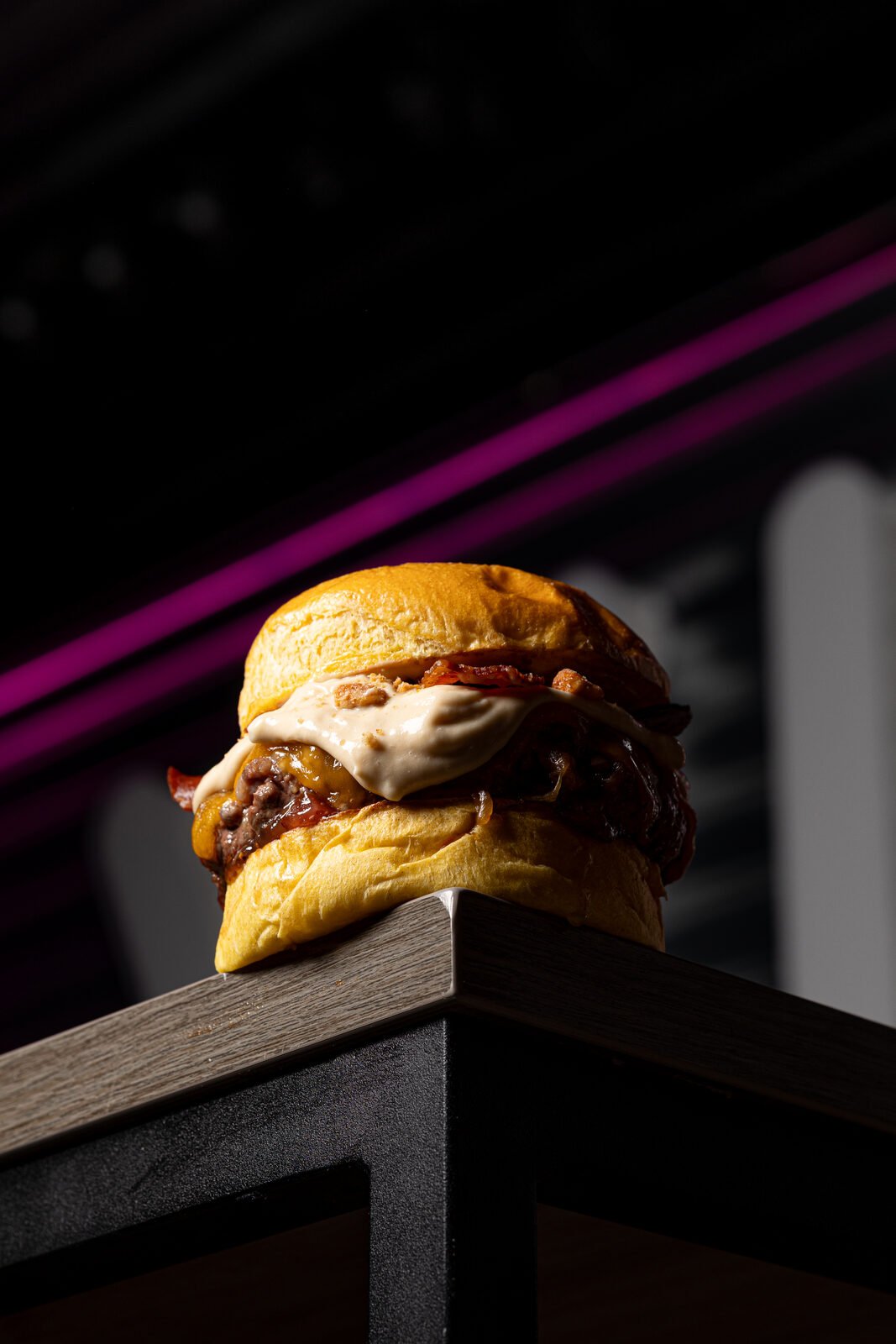 Smash burger doble con bacon y salsa cremosa sobre mesa con neón magenta de fondo