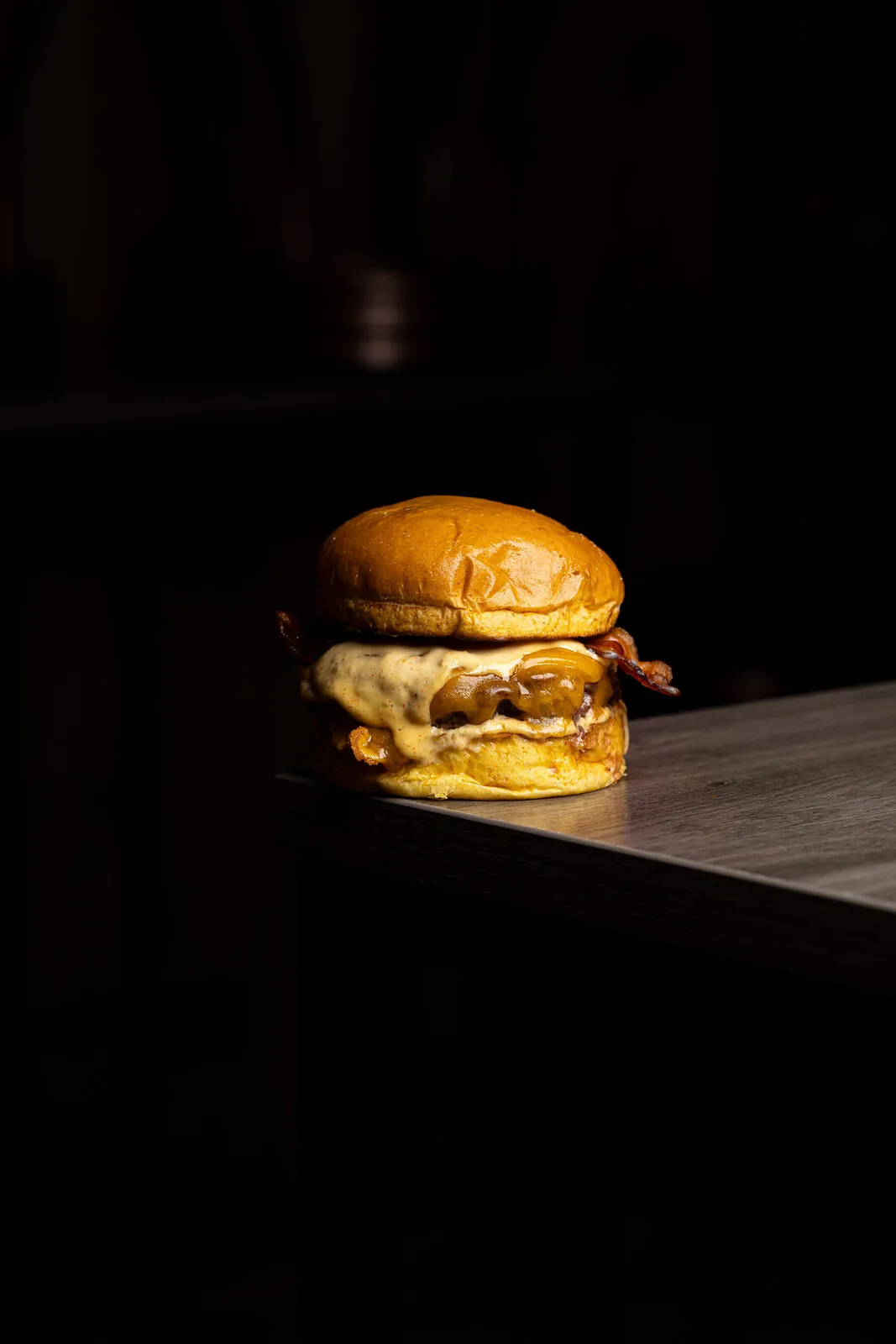 Smash burger con bacon iluminada en spotlight cinematográfico sobre fondo negro
